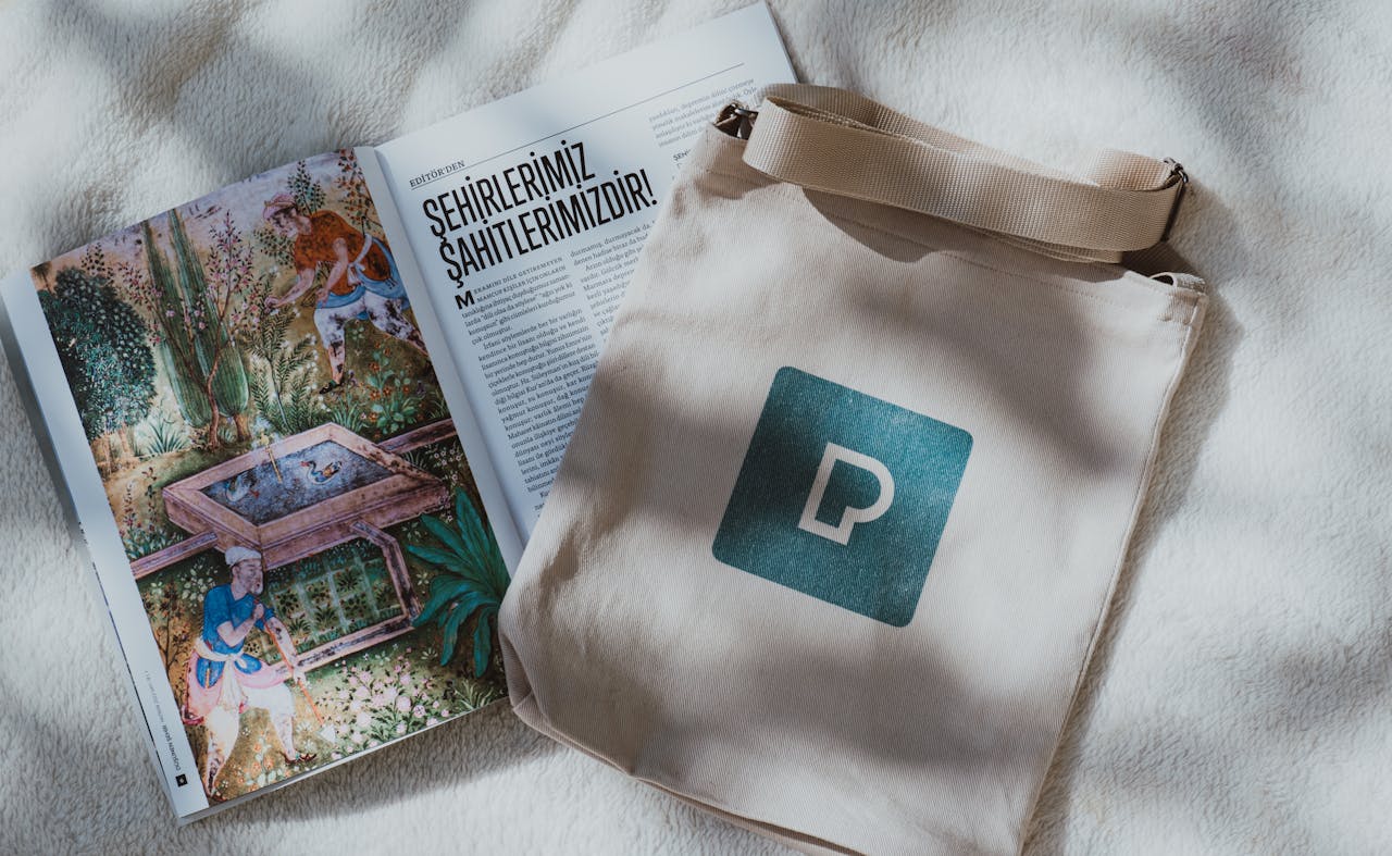 gallery-5 Open illustrated magazine with canvas tote bag on a soft fabric surface, displaying text in Turkish.